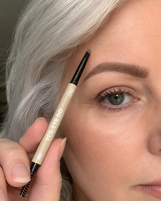 Silver-haired woman holding the Grey Micro Brow Pencil up beside her groomed brow