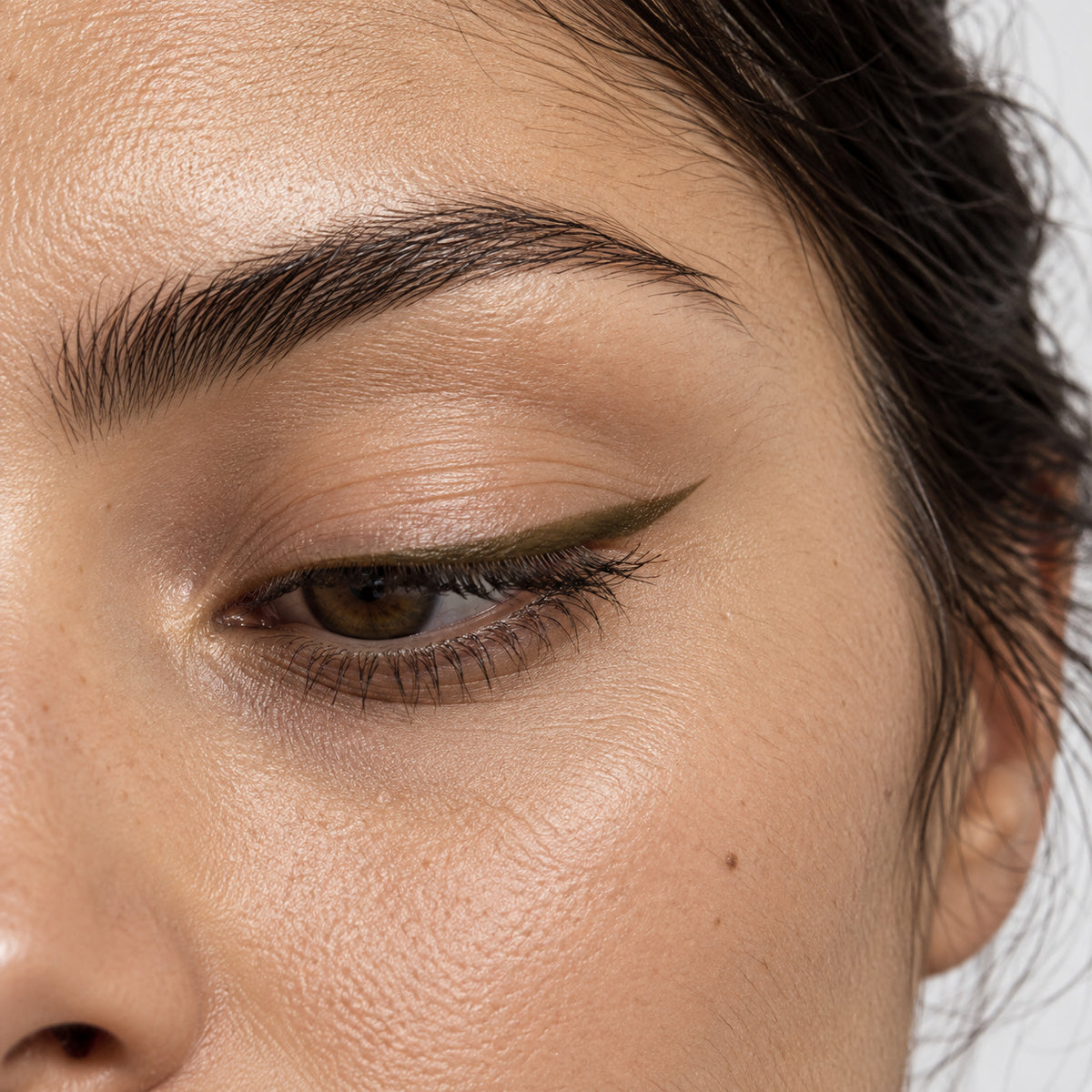 Eye close-up with a thin olive-brown winged liner extending from the outer corner