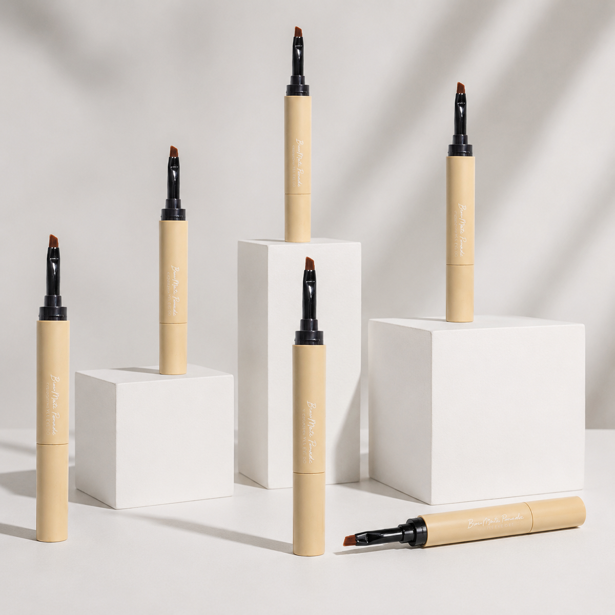 Six brow pomade pens arranged on white display blocks