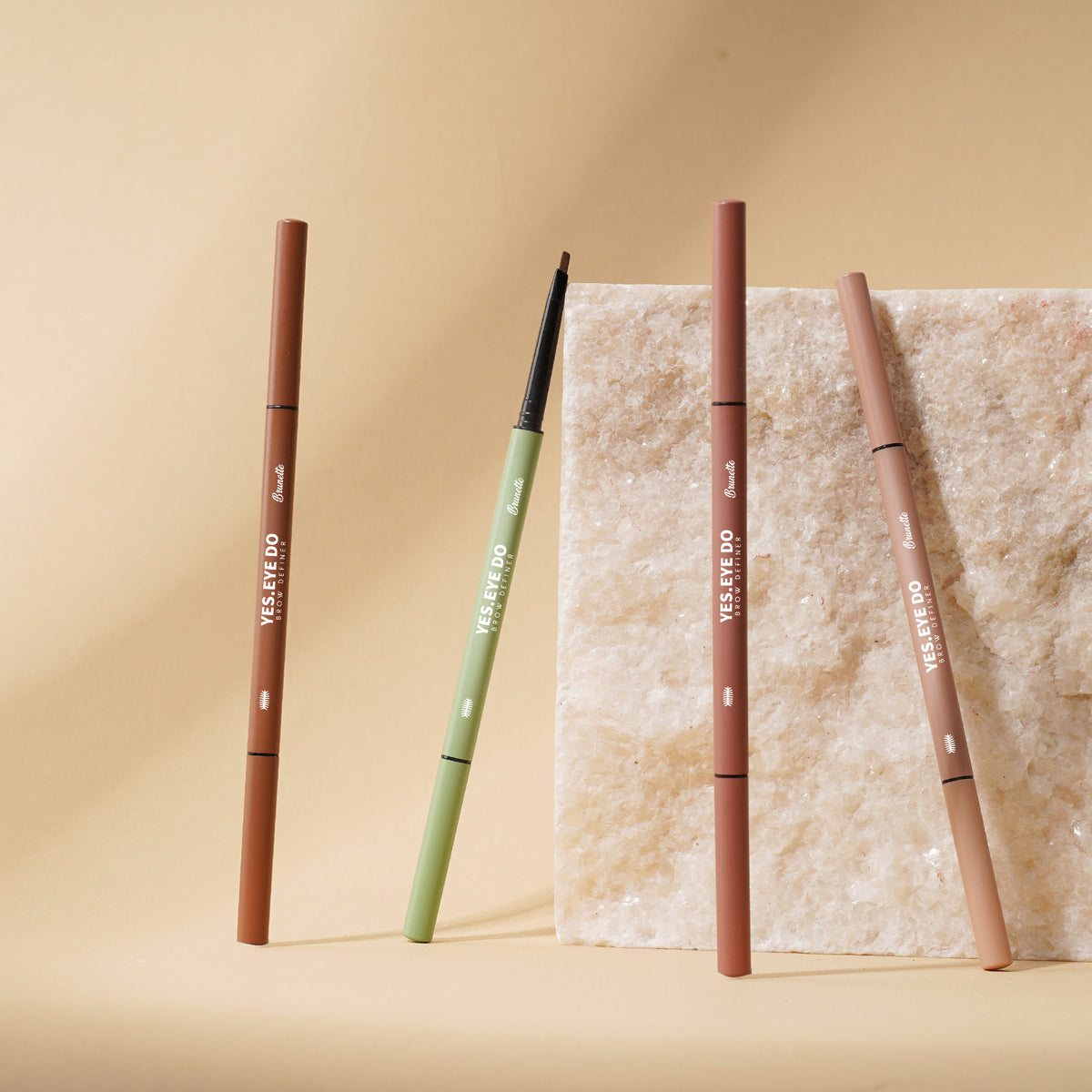 Three Micro Brow Pencils standing by a stone block in brown, green and pink cases
