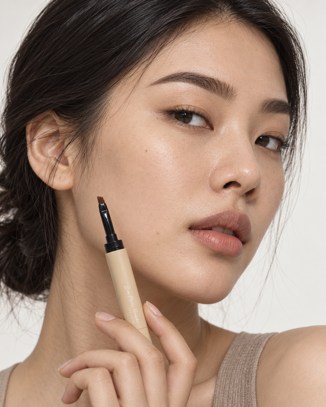 Model holding the beige Brow Mate Pomade pen, close-up beauty portrait