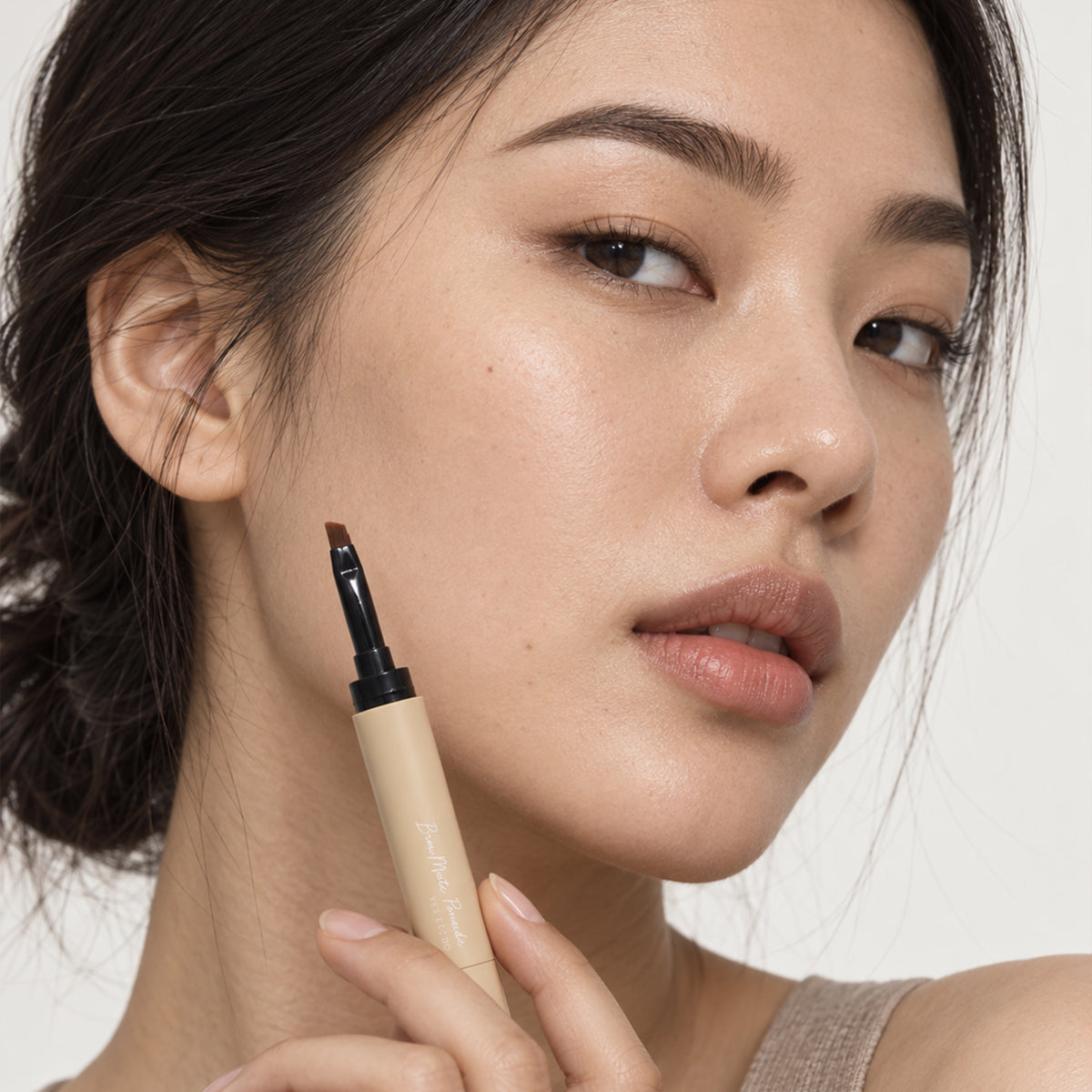 Model holding the 2-in-1 Brow Pomade Pen with the angled brush extended