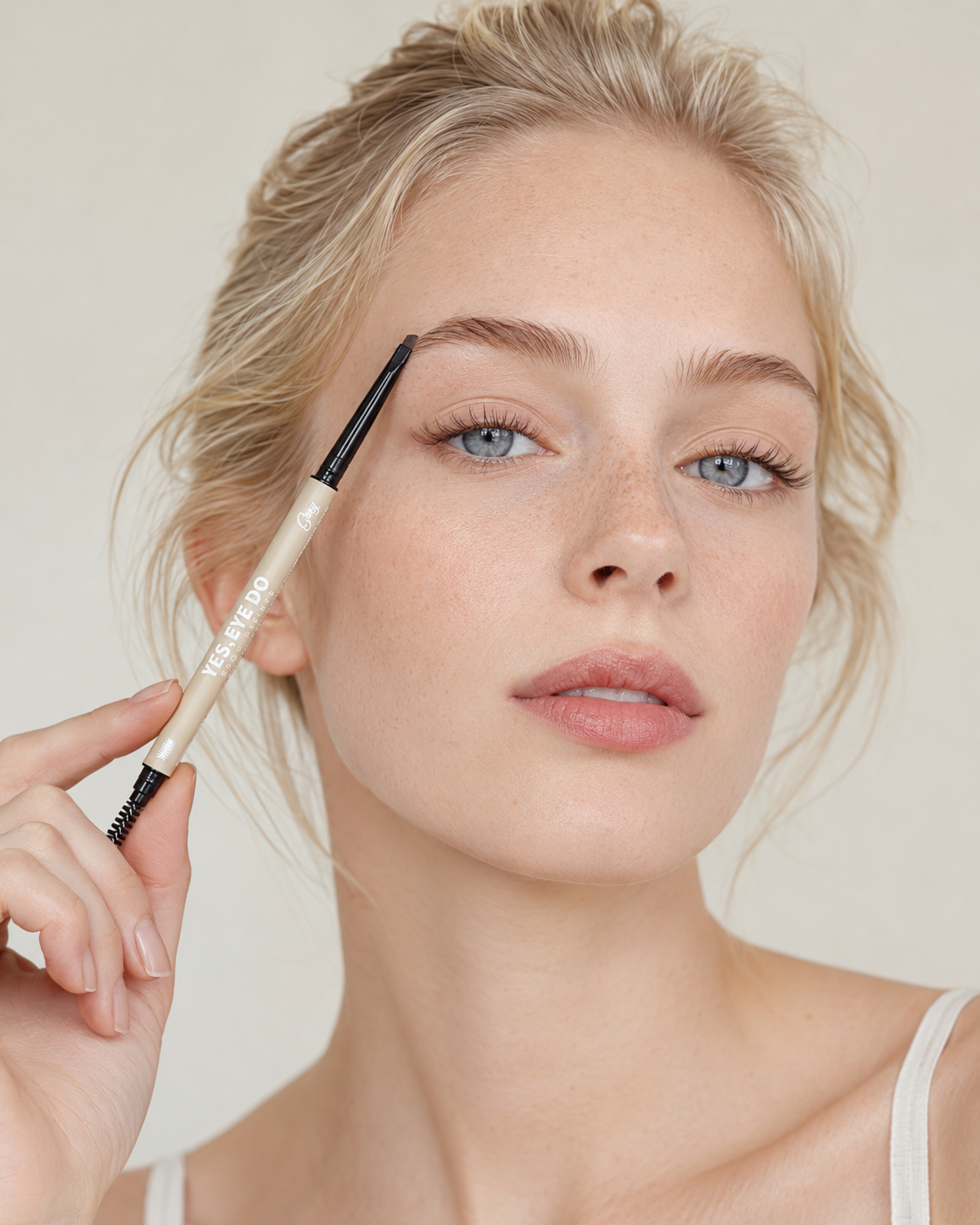 Blonde model holding the micro brow pencil to her brow