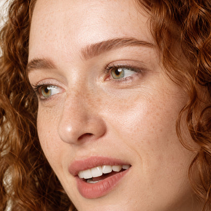 Close-up of dark auburn brow hairs and green eyes on fair freckled skin