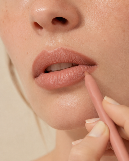 Close-up of a hand applying nude lip liner along the corner of the lower lip