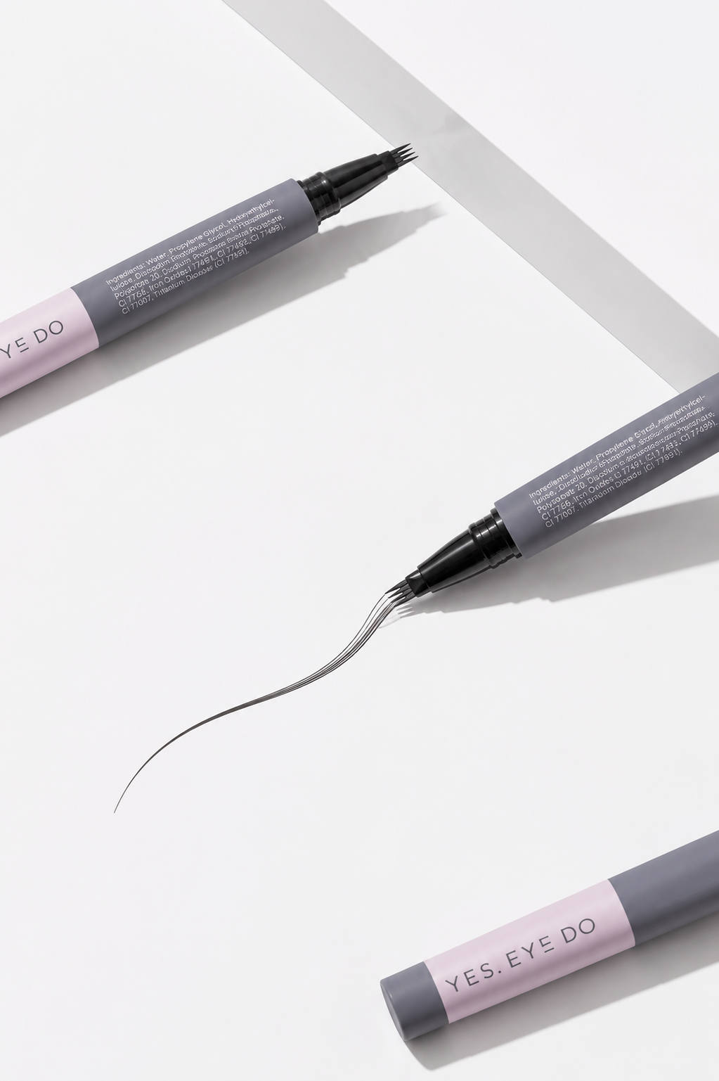 Three 4-prong brow pens arranged diagonally, with the uncapped tip drawing a long tapered stroke